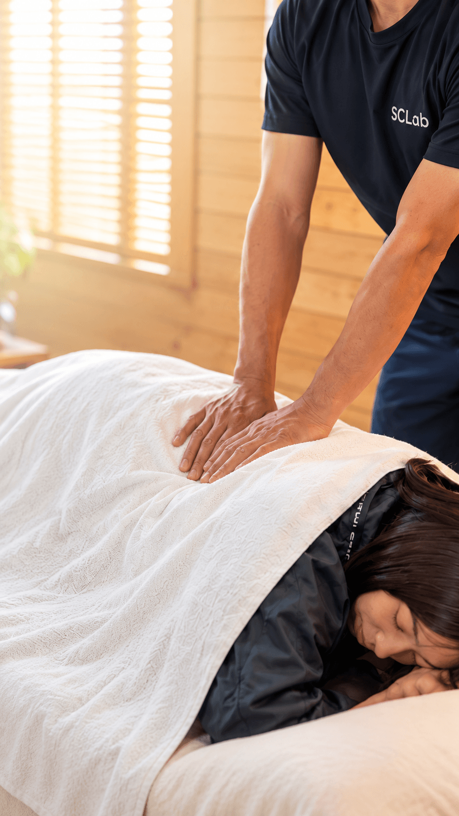 うつ伏せの利用者の背部に両手を当てて施術するSCLabのトレーナー